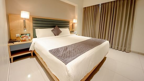 An image of a bedroom with double size bed and bedside table with lamps on either side - Pride Resort Ambaji